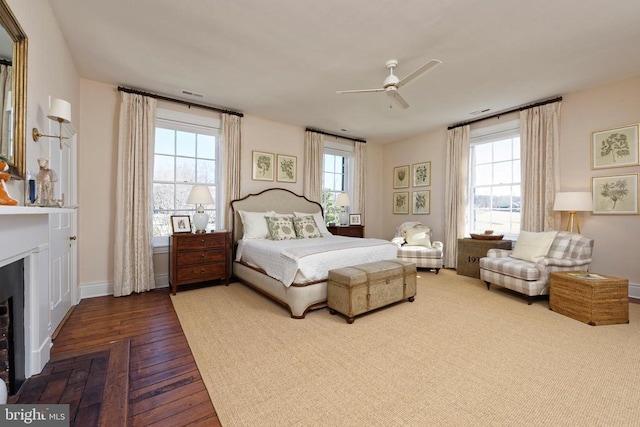 bedroom featuring wood finished floors, visible vents, a fireplace, a ceiling fan, and baseboards