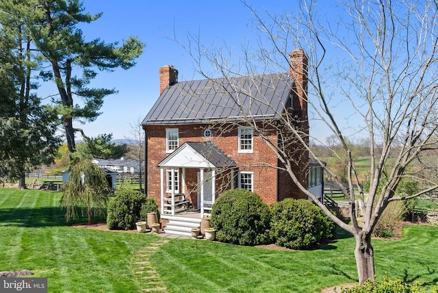 view of front of house with brick siding, a front lawn, a standing seam roof, and a chimney