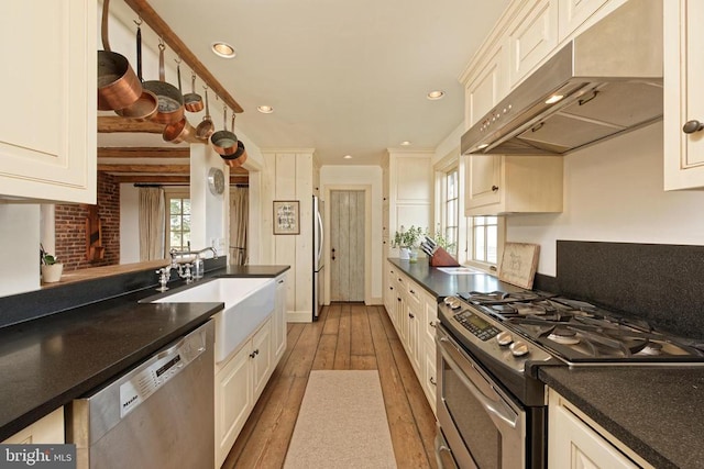 kitchen with dark countertops, stainless steel appliances, hardwood / wood-style floors, and under cabinet range hood