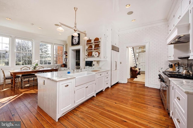 kitchen featuring light wood finished floors, a peninsula, a sink, high quality appliances, and white cabinetry