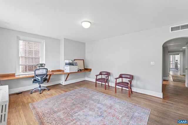 office featuring arched walkways, baseboards, visible vents, and wood finished floors