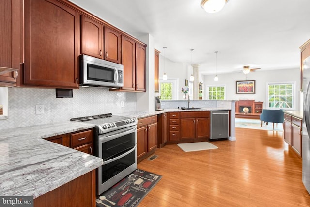 kitchen featuring a peninsula, light wood-style flooring, a sink, stainless steel appliances, and decorative backsplash