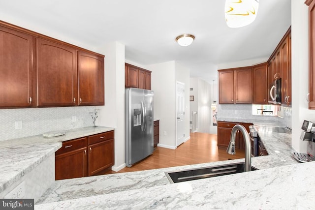 kitchen featuring a sink, stainless steel appliances, light stone counters, light wood-type flooring, and backsplash