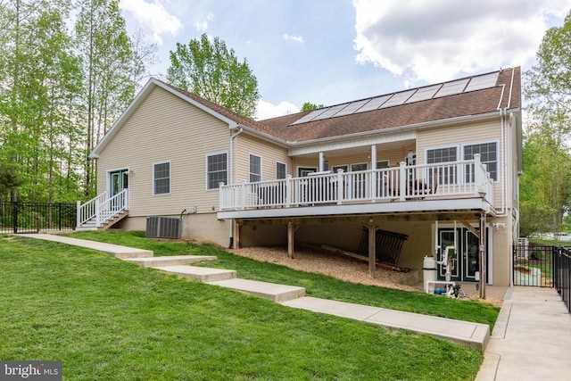 rear view of house with central air condition unit, roof mounted solar panels, a yard, and a deck