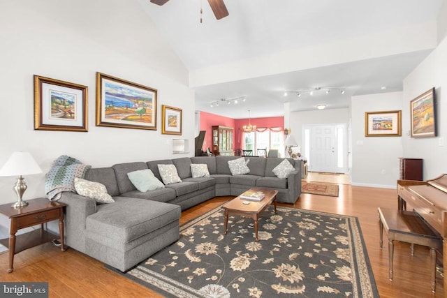 living area featuring a ceiling fan, baseboards, rail lighting, vaulted ceiling, and wood finished floors
