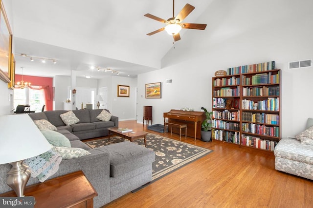 living room featuring wood finished floors, ceiling fan with notable chandelier, track lighting, visible vents, and lofted ceiling