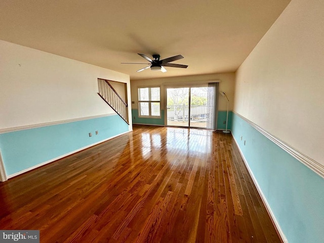 unfurnished room featuring a ceiling fan, wood finished floors, baseboards, and stairs