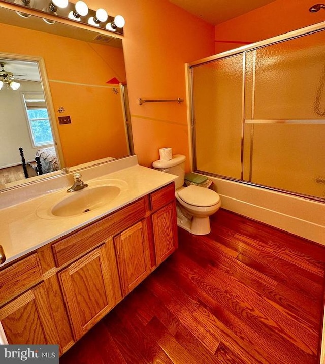 full bathroom with connected bathroom, wood finished floors, shower / bath combination with glass door, vanity, and toilet