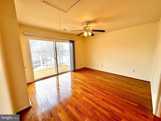 unfurnished room with attic access, wood finished floors, ceiling fan, and baseboards