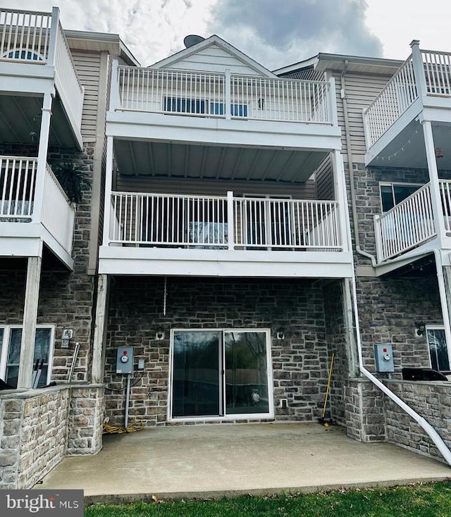 rear view of house featuring a balcony, stone siding, and a patio area