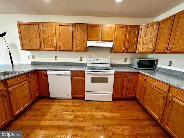 kitchen with white appliances, under cabinet range hood, brown cabinets, and dark wood-style flooring