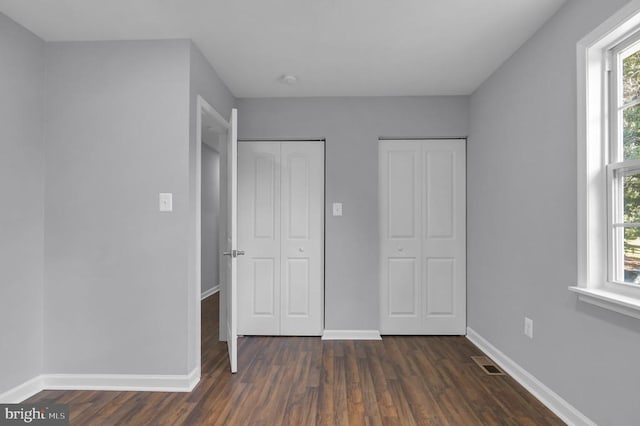 - unfurnished bedroom with dark wood-style floors and two closets