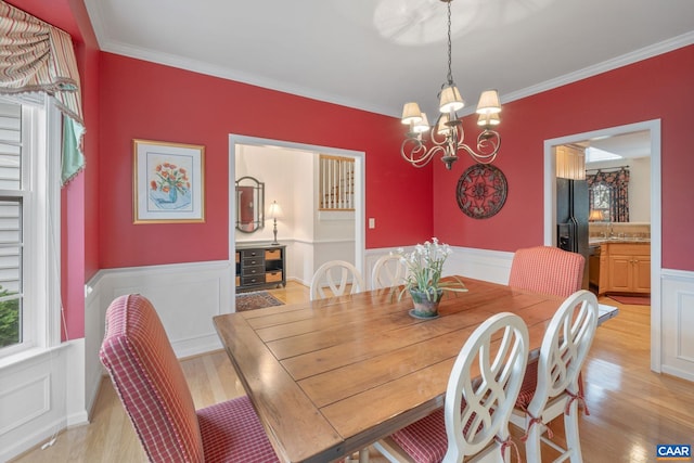 dining space featuring ornamental molding, a notable chandelier, wainscoting, and light wood-style floors