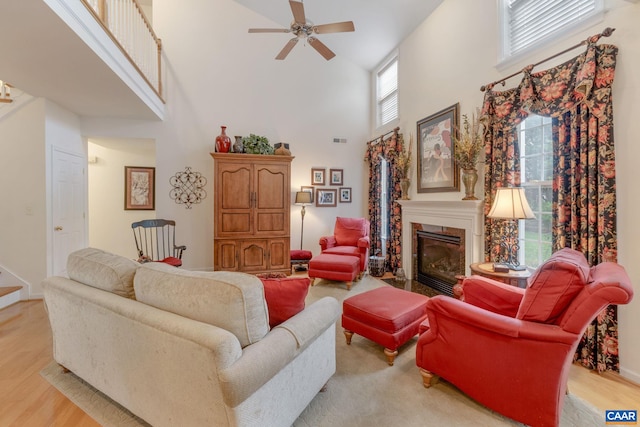 living area featuring ceiling fan, light wood-type flooring, a towering ceiling, and a fireplace with flush hearth