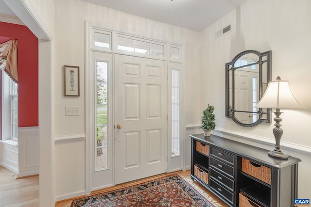 foyer entrance with light wood-type flooring, a wealth of natural light, visible vents, and a wainscoted wall