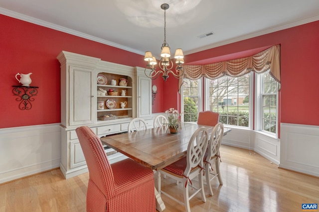dining room featuring ornamental molding, a notable chandelier, a wainscoted wall, and visible vents