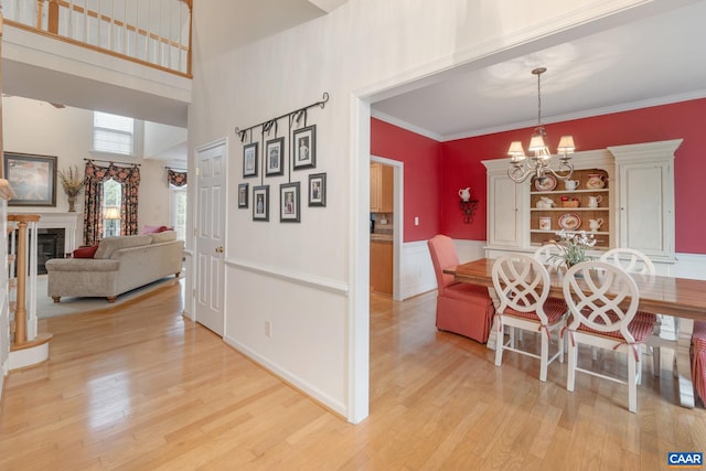 dining area with wood finished floors, a towering ceiling, a chandelier, crown molding, and a glass covered fireplace
