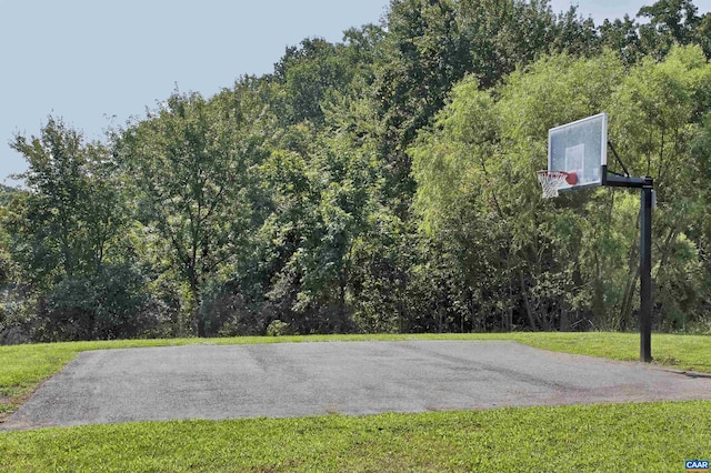 view of sport court with basketball court, a view of trees, and a lawn