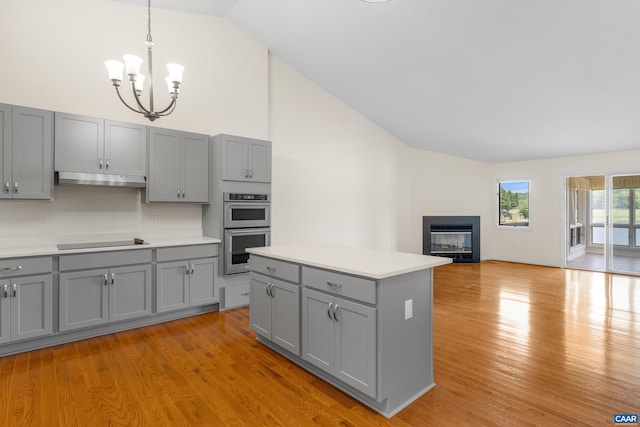 kitchen with double oven, gray cabinets, a glass covered fireplace, light countertops, and a chandelier