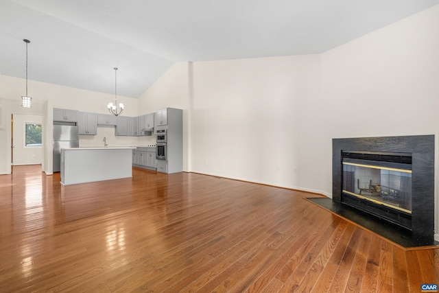 unfurnished living room featuring a sink, wood finished floors, high vaulted ceiling, an inviting chandelier, and a glass covered fireplace