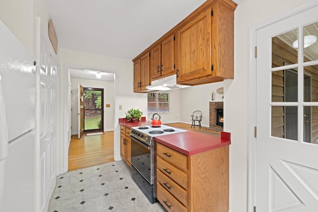 409 Thomas St, Staunton, VA 24401 - kitchen featuring electric stove, under cabinet range hood, a brick fireplace, brown cabinetry, and freestanding refrigerator