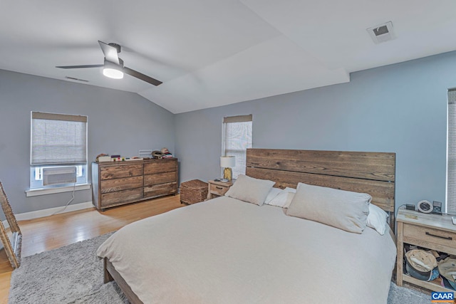 bedroom with wood finished floors, multiple windows, cooling unit, vaulted ceiling, and baseboards