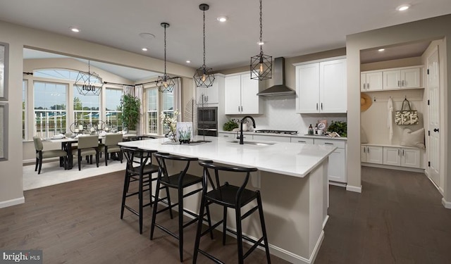 kitchen with wall chimney exhaust hood, a sink, dark wood-type flooring, light countertops, and a breakfast bar area