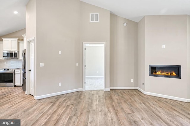 unfurnished living room featuring light wood finished floors, high vaulted ceiling, visible vents, baseboards, and a glass covered fireplace