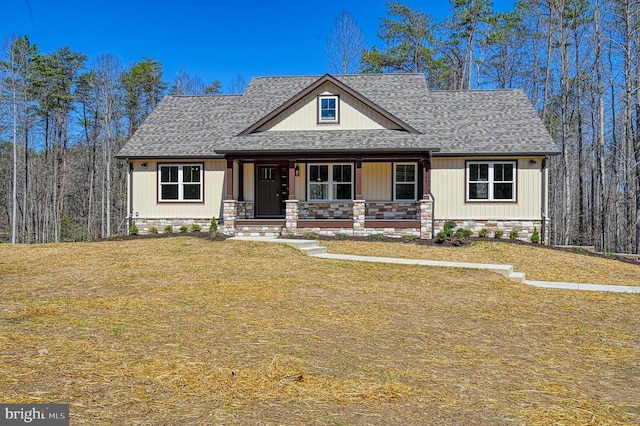 view of front facade with covered porch, roof with shingles, and a front lawn