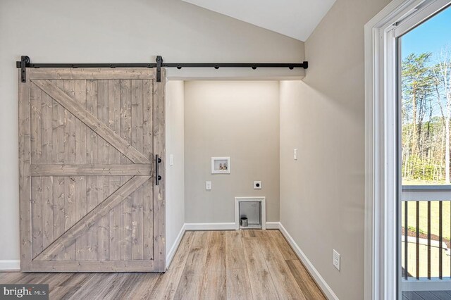 clothes washing area with hookup for a washing machine, wood finished floors, a barn door, and electric dryer hookup