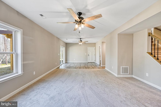 carpeted spare room with baseboards, ceiling fan, stairway, and visible vents