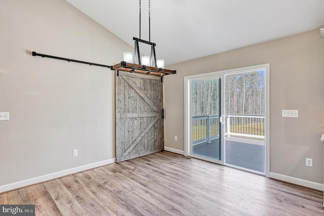 unfurnished dining area featuring a barn door, wood finished floors, baseboards, and lofted ceiling