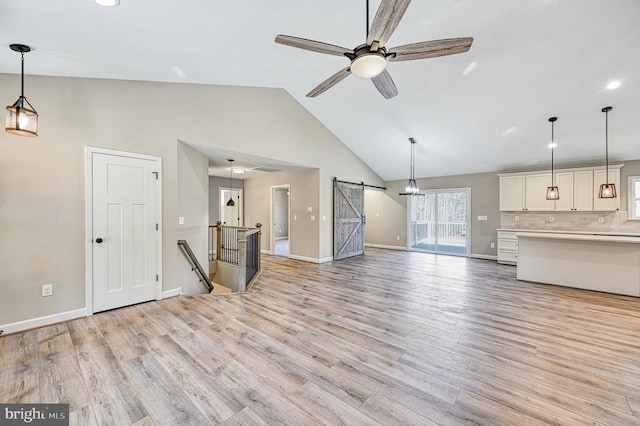 unfurnished living room with a barn door, high vaulted ceiling, light wood-style flooring, a ceiling fan, and baseboards