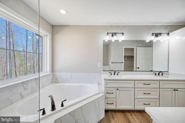 full bathroom featuring a sink, double vanity, a garden tub, and wood finished floors