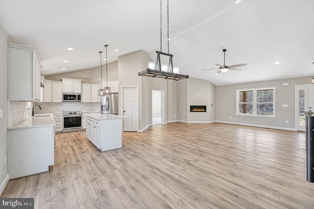 kitchen with ceiling fan with notable chandelier, stainless steel appliances, white cabinets, light countertops, and a kitchen island