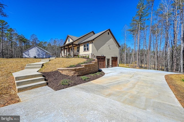 view of side of property with covered porch, driveway, a garage, and stairs