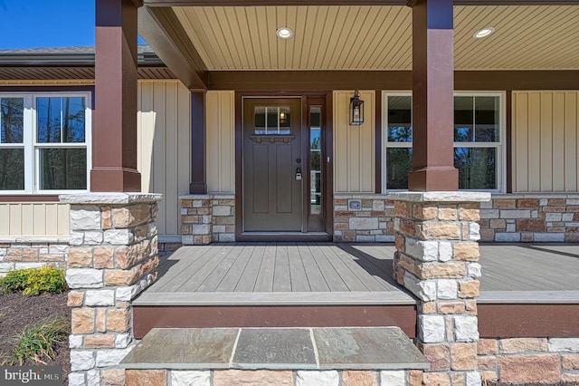 view of exterior entry with a porch, stone siding, and board and batten siding
