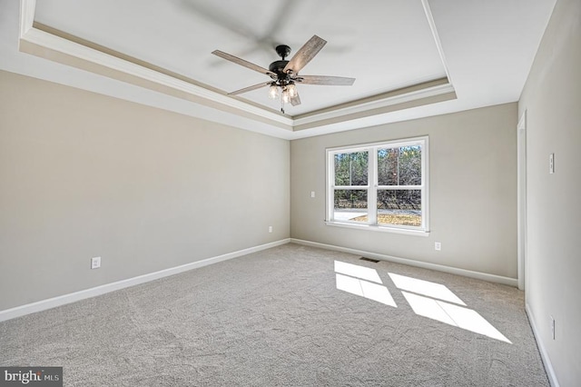 spare room featuring carpet flooring, a tray ceiling, visible vents, baseboards, and ceiling fan