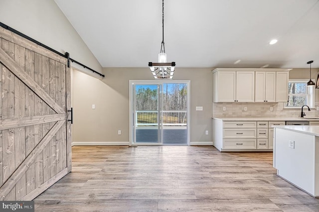 kitchen with a barn door, light wood-type flooring, white cabinetry, light countertops, and hanging light fixtures