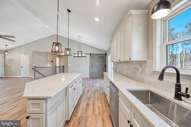 kitchen with lofted ceiling, dishwasher, light wood finished floors, a sink, and white cabinets