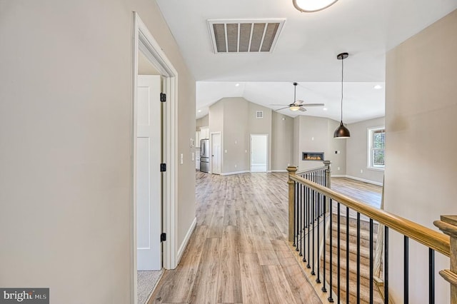 hall with lofted ceiling, light wood-style flooring, baseboards, and visible vents