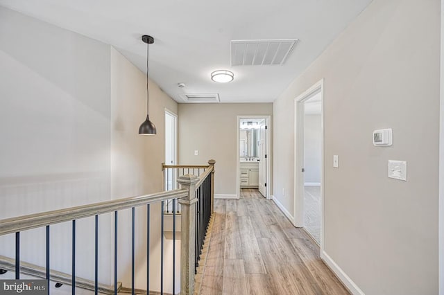hall featuring baseboards, light wood-style floors, an upstairs landing, and visible vents