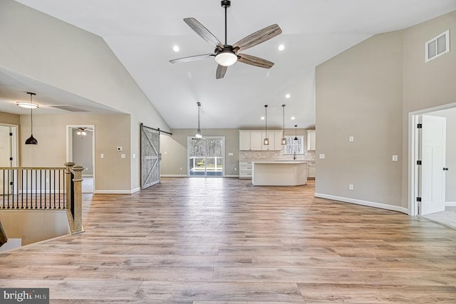 unfurnished living room with a ceiling fan, a barn door, visible vents, and high vaulted ceiling