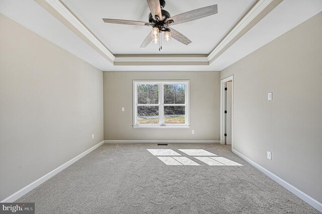 carpeted spare room with a tray ceiling, ceiling fan, crown molding, and baseboards