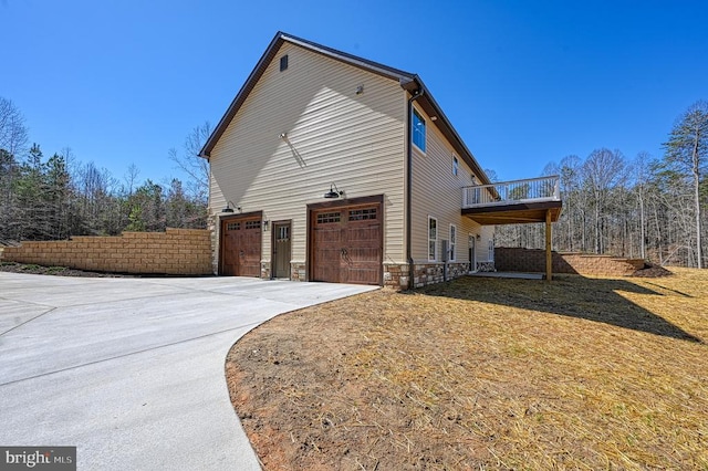 view of side of property with concrete driveway, stone siding, an attached garage, and fence