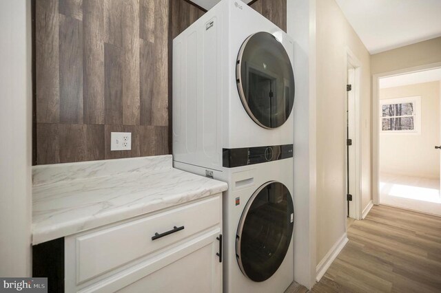 laundry area featuring stacked washer / dryer, cabinet space, light wood-type flooring, and baseboards