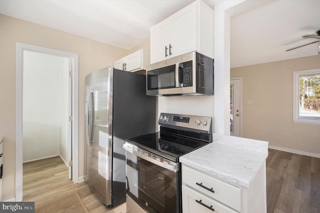 kitchen with stainless steel appliances, light wood-style flooring, white cabinets, and light stone countertops
