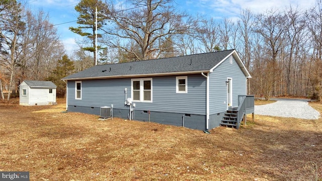 rear view of house with an outbuilding, a shingled roof, a storage shed, central AC unit, and crawl space