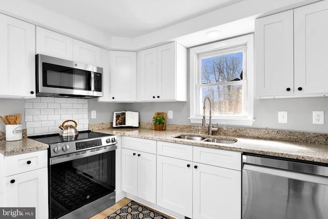 kitchen with light stone counters, backsplash, appliances with stainless steel finishes, white cabinetry, and a sink