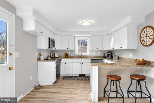 kitchen featuring stainless steel appliances, light wood-style flooring, white cabinetry, a sink, and a peninsula